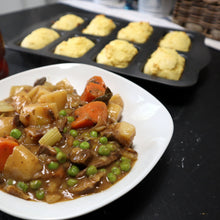 Cargar imagen en el visor de la galería, Stew with carrots and peas on a white plate, with a bottle of honey in the background.