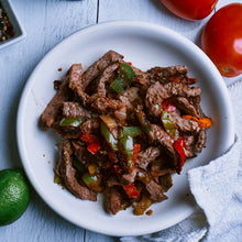 Cargar imagen en el visor de la galería, A plate of cooked Beef Wagyu Fajita Meat with vegetables, next to a lime, avocado, and a dish of spices.