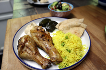 Cargar imagen en el visor de la galería, Plated dish with chicken, yellow rice, and pita bread on a wooden table.

